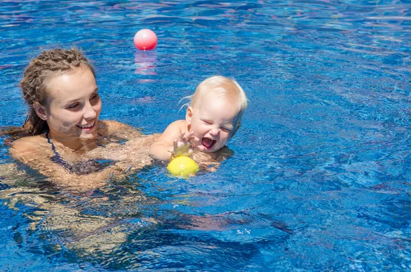 Madre y su hijo en la piscina. Mujer jugando con una pelota con su hijita . — Foto de Stock