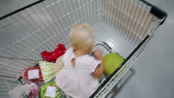Un niño en un carrito de compras en un supermercado . — Vídeo de stock