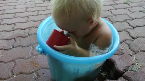 Bebê está tomando banho em um balde de água . — Vídeo de Stock