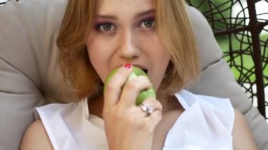 Beyaz elbiseli bir kız bir yeşil elma yiyor.