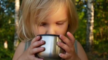 Çocuk sonbahar ormanda çay içiyor.