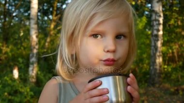 Çocuk sonbahar ormanda çay içiyor.