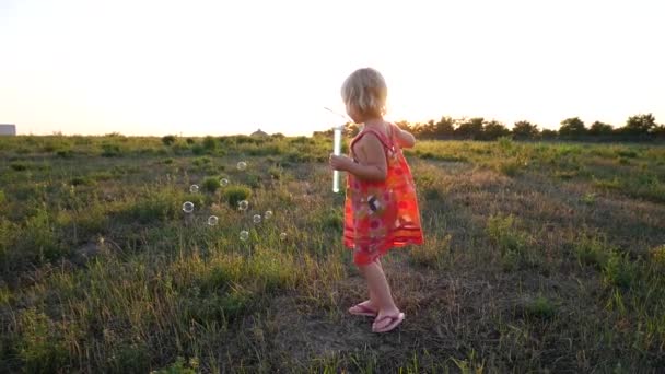 En flicka som blåser såpbubblor i strålar från en solnedgång. — Stockvideo