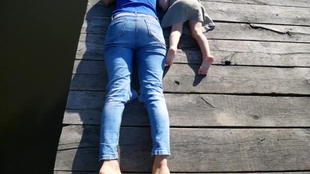 Mom and daughter lie on the pier and enjoy nature. The video is shot from above, the camera flies above them. — Stock Video