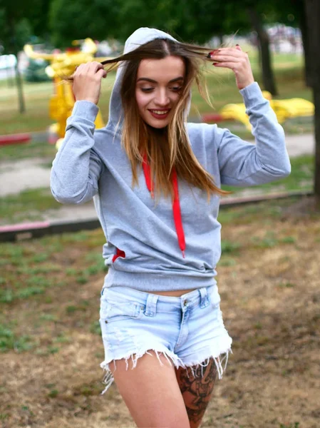 Seductive young woman in short denim shorts. Sexy photosession in the park. — Stock Photo, Image