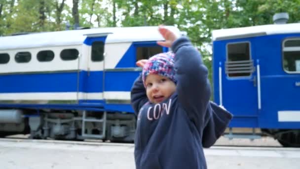 La niña está escoltando el tren a la estación. El niño agitando su mano al tren que sale . — Vídeos de Stock