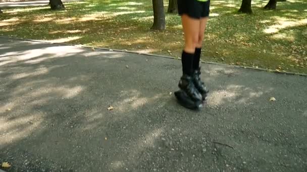 Молодая красивая девушка занимается спортом в парке. Женщина прыгает на специальной обуви для фитнеса . — стоковое видео