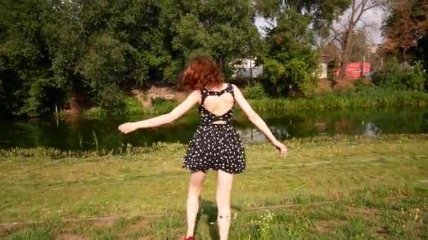 Een jonge vrouw in korte rok jurk loopt aan de oever van een vijver. Het meisje is spinnen en plezier. — Stockvideo
