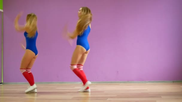 Due ragazze in costume da bagno blu danzano sullo sfondo di un muro viola. Le ragazze in stile disco stanno ballando sexy . — Video Stock