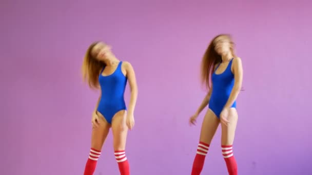 Vor dem Hintergrund einer lila Wand tanzen zwei Mädchen in blauen Badeanzügen. Mädchen im Disco-Stil tanzen sexy. — Stockvideo