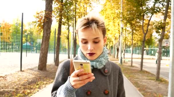 Kız parkta yürüyor ve Internet üzerinde iletişim kurar. Bir kadın bir smartphone sokakta haber okur. — Stok video