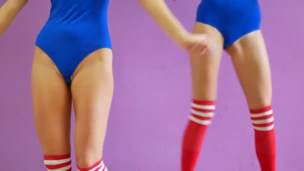 Twee meisjes in blauwe badpakken dansen tegen de achtergrond van een paarse muur. Meisjes in de disco stijl dansen sexy. — Stockvideo