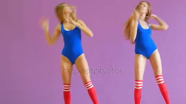 Dos chicas en trajes de baño azules bailan sobre el fondo de una pared púrpura. Las niñas en el estilo disco están bailando sexy . — Vídeos de Stock