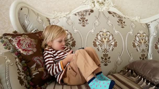 A gyermek néz rajzfilmeket a telefon. Egy gyerek, egy vintage székre. — Stock videók