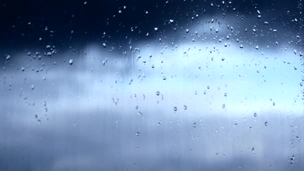 Rain drops on the window. Outside the window you can see how the clouds are floating in the defocus — Stockvideo
