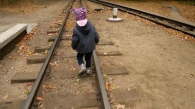 Küçük bir kız raylar üzerinde yürüyor. Sonbahar orman.