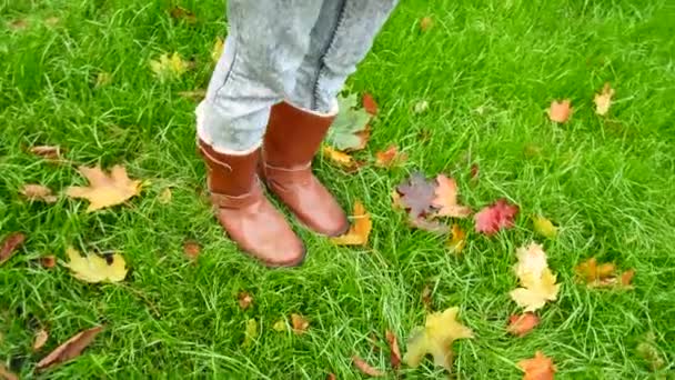 Gambe femminili in stivali su uno sfondo di erba verde e foglie cadute — Video Stock