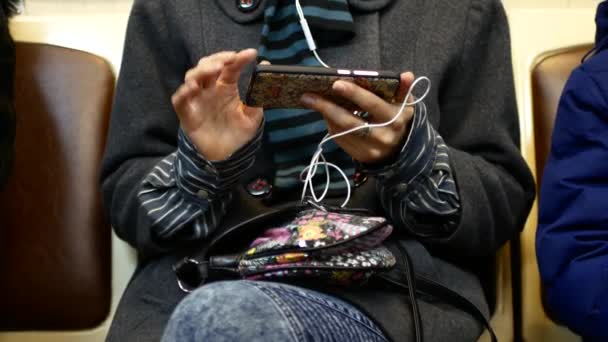 Девушка слушает музыку или смотрит видео на смартфоне в вагоне метро — стоковое видео