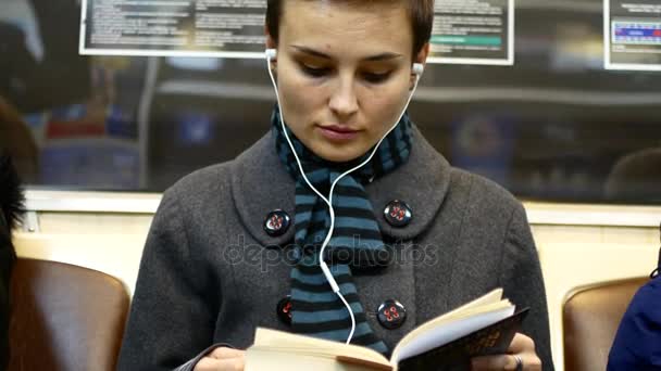 Девушка в наушниках читает книгу в метро — стоковое видео