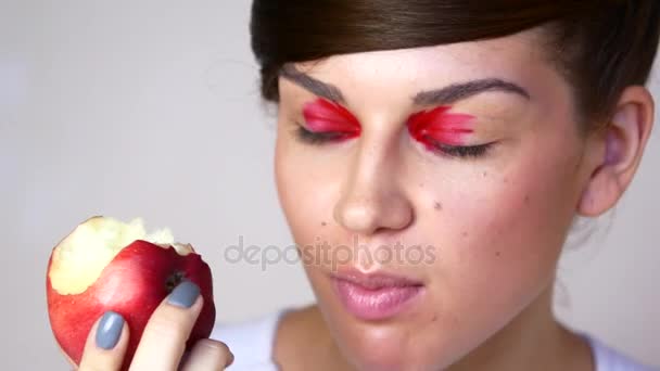 Une belle fille avec un maquillage lumineux mâche une pomme rouge — Video