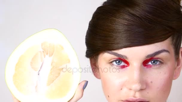 Portret van een jonge vrouw op een witte achtergrond. Een meisje heeft half een pomelo — Stockvideo
