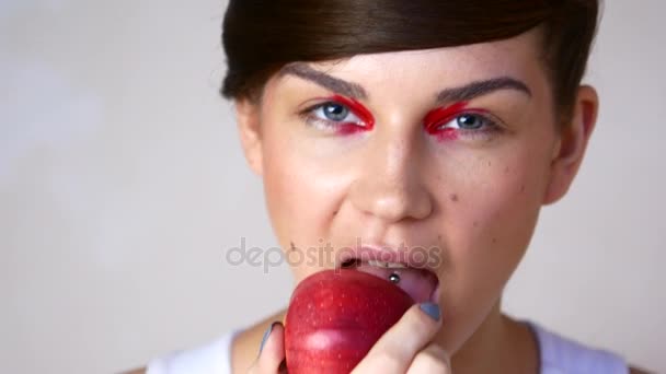 Una joven con maquillaje de moda mastica una manzana — Vídeos de Stock