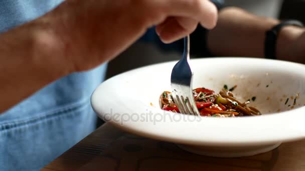 Un hombre está comiendo fideos asiáticos con verduras con un tenedor — Vídeos de Stock