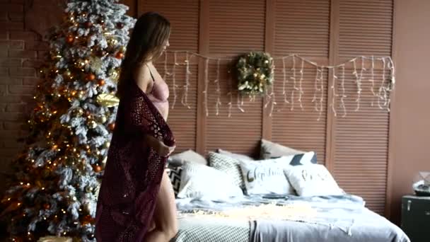 Sexy Mädchen geht zum Fenster am Weihnachtsbaum vorbei. die Frau geht und zieht sich schön aus — Stockvideo