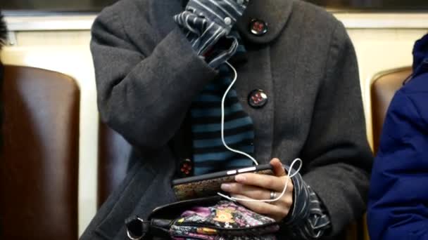 Une fille écoute de la musique ou regarde des vidéos sur un smartphone dans une voiture de métro — Video