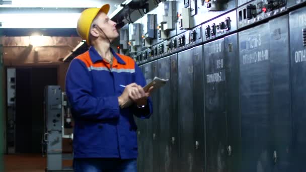 Працівник фіксує показання лічильників на електростанції. Чоловік в шоломі і робочий халат — стокове відео