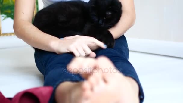 Молода красива дівчина відпочиває у своїй квартирі. Чорний кіт сидить на руках жінки — стокове відео