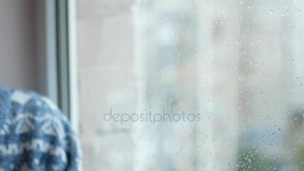Uma mulher triste senta-se e olha pela janela. Está chovendo lá fora. — Vídeo de Stock