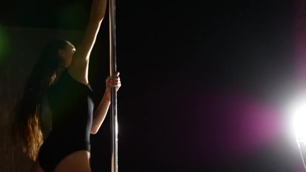 A pólus közelében egy gyönyörű és szexi nő táncol. Videó a sötét színek, a lány mozgó van meleg, keretek alkalmas létesítmény — Stock videók