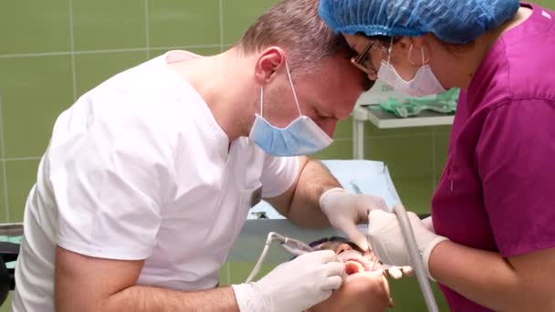 Een tandarts met een assistent verwijdert de tand van een jonge vrouw — Stockvideo