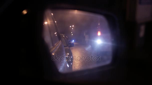 Kaca spion mobil basah. Lalu lintas kota malam hari. Mobil ambulan di cermin. — Stok Video