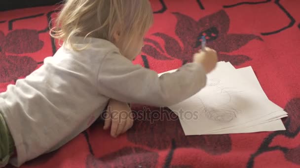 La ragazza sta disegnando sdraiata sul tappeto rosso . — Video Stock