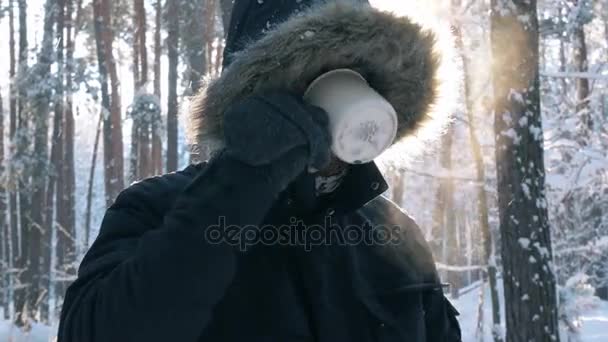 Ένας νεαρός άνδρας πίνοντας ένα ζεστό τσάι σε ένα δάσος του χειμώνα. Όμορφο ηλιόλουστο πρωί μέσα στο δάσος του χειμώνα. έννοια χαλάρωση στη φύση. — Αρχείο Βίντεο