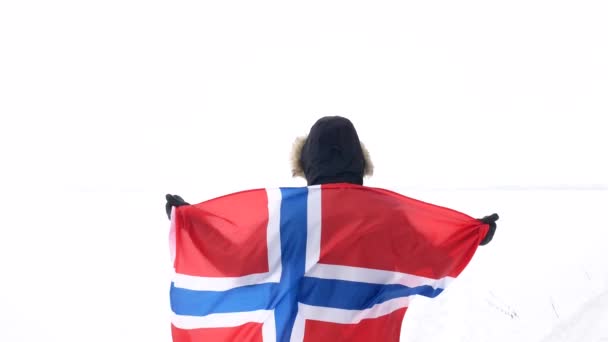 Un uomo con la bandiera della Norvegia sta con le spalle su un campo innevato . — Video Stock
