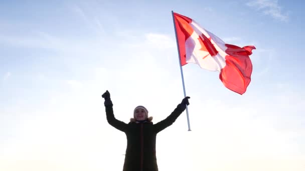 Jonge vrouw zwaaien van een vlag van Canada tegen een blauwe hemel. Ventilator ondersteuning. — Stockvideo