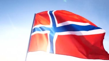 Kırmızı mavi çapraz Norveç ulusal bayrak ile yavaş yavaş beyaz bayrak direği üzerinde açık mavi gökyüzünde sallıyor.