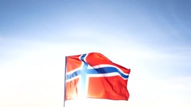 Kırmızı mavi çapraz Norveç ulusal bayrak ile yavaş yavaş beyaz bayrak direği üzerinde açık mavi gökyüzünde sallıyor.