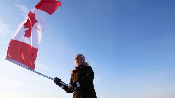 Jonge vrouw zwaaien van een vlag van Canada tegen een blauwe hemel. Ventilator ondersteuning. — Stockvideo