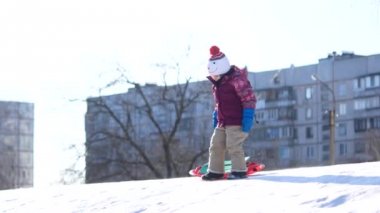 Çocuk bir kış yürüyüş. Bir kız bir plastik plaka üzerinde bir kar slayttan biniyor.