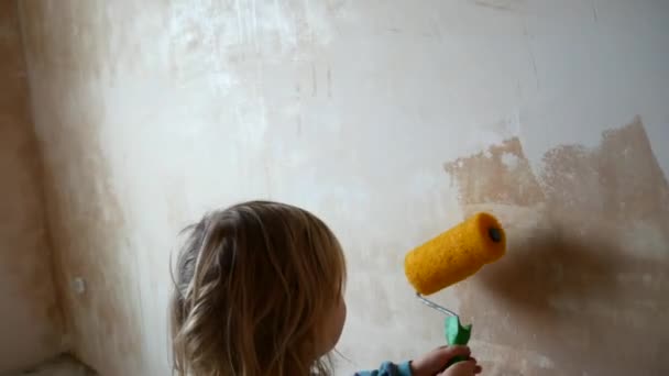 Το κορίτσι σας βοηθά να κάνετε επισκευές στο δωμάτιό της. Το παιδί ζωγραφίζει τους τοίχους με έναν κύλινδρο. — Αρχείο Βίντεο