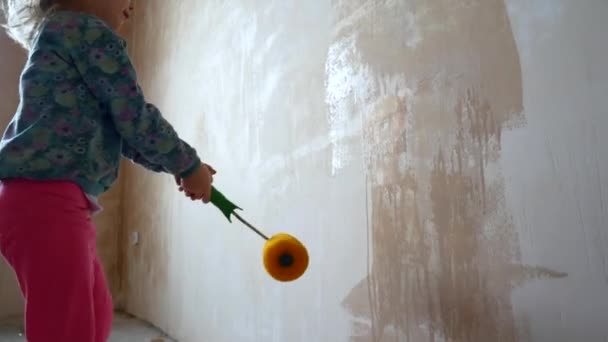 Flickan hjälper till att göra reparationer i sitt rum. Barnet målar väggarna med en roller. — Stockvideo