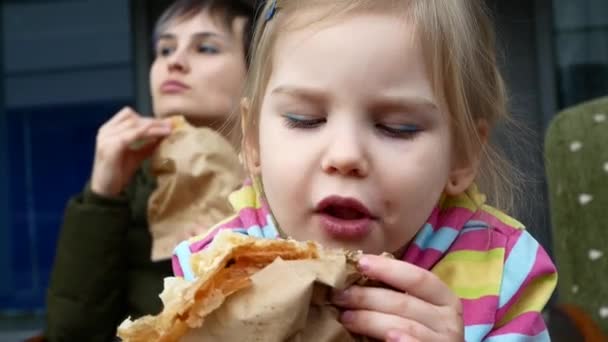 Moeder en dochter zijn het eten van een croissant. Delicious straat voedsel, familie waarden. — Stockvideo