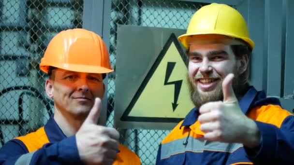 Двое электриков на подстанции улыбаются возле знака опасности — стоковое видео