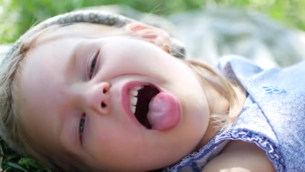 Primer plano de la niña acostada en la manta de picnic y sacando la lengua — Vídeos de Stock