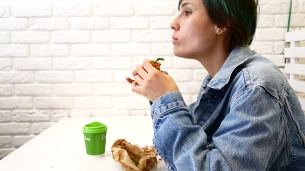 Женщина ест сэндвич, сидит у окна в кафе — стоковое видео