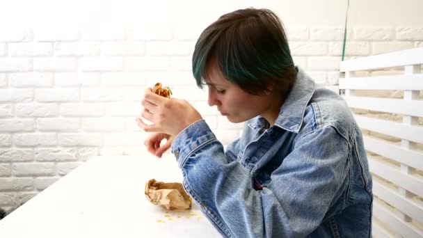 Mujer comiendo sándwich, sentada cerca de la ventana en el café — Vídeos de Stock